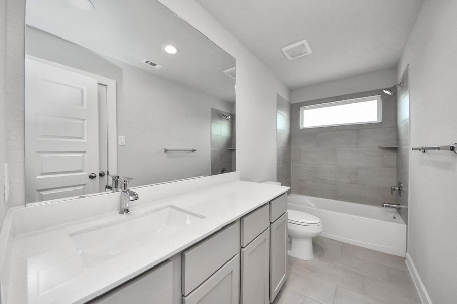 Secondary bath features tile flooring, bath/shower combo with tile surround, light stained wood cabinets, beautiful light countertop. Sample photo of completed home with similar floor plan. Actual colors and selections may vary.