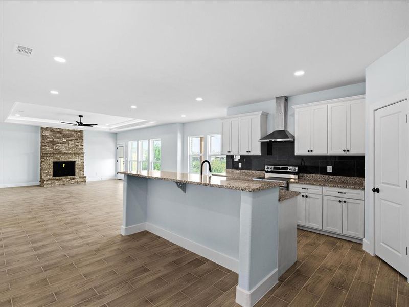 Kitchen with dark wood-style flooring, ceiling fan, wall chimney exhaust hood, a kitchen island with sink, and white cabinets