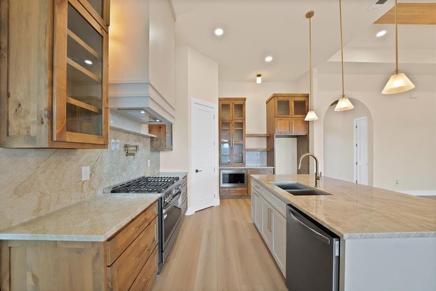 Kitchen with glass insert cabinets, decorative light fixtures, light stone countertops, appliances with stainless steel finishes, and tasteful backsplash Kitchen with glass insert cabinets, decorative light fixtures, light stone countertops, appliances with stainless steel finishes, and tasteful backsplash