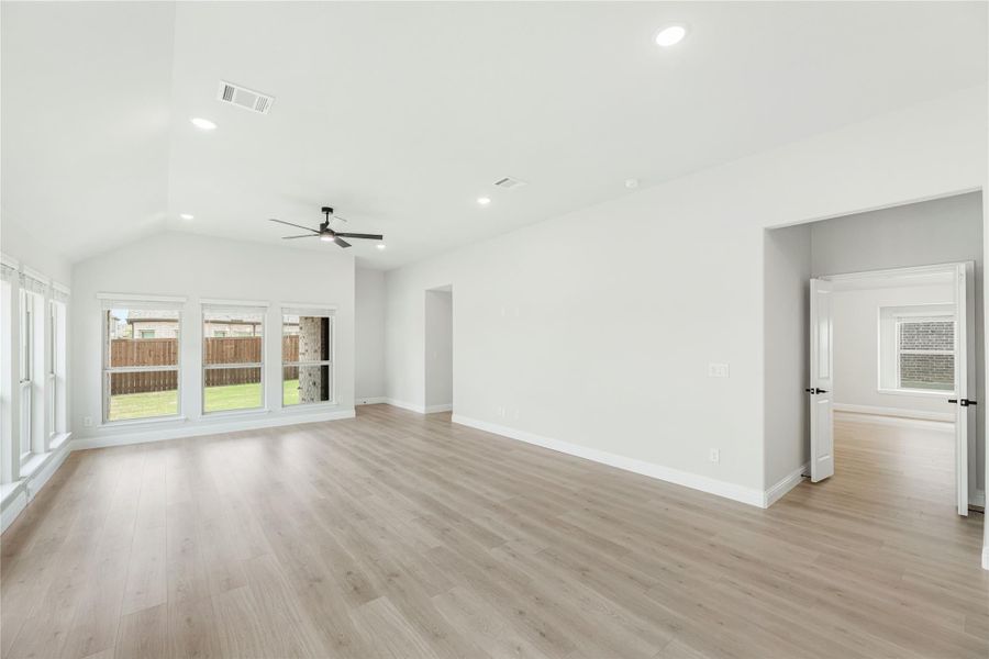 Open living room with vaulted ceiling, ceiling fan, light wood floors, and large backyard-facing windows