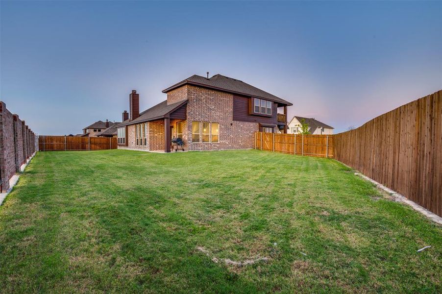 Back of property at dusk with brick siding, a chimney, and a fenced backyard Back of property at dusk with brick siding, a chimney, and a fenced backyard