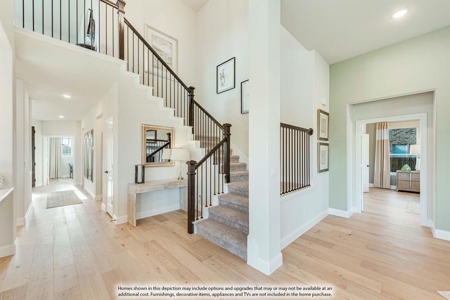 Two-story foyer with carpeted staircase, dark iron railings, and light hardwood floors