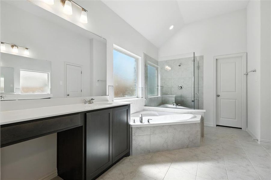 Bathroom with a stall shower, a garden tub, vanity, vaulted ceiling, and light tile patterned flooring