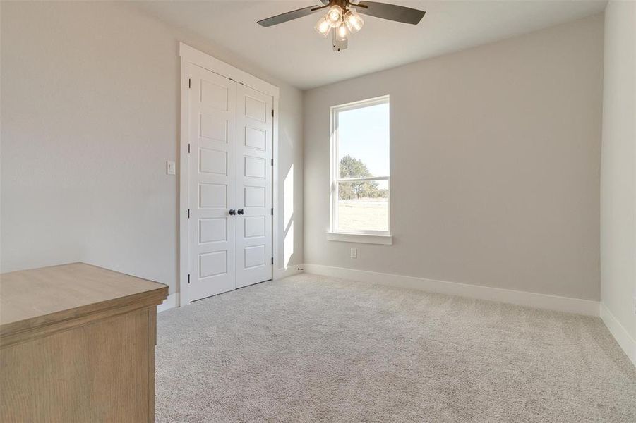 Empty room featuring ceiling fan, light colored carpet, and a wealth of natural light