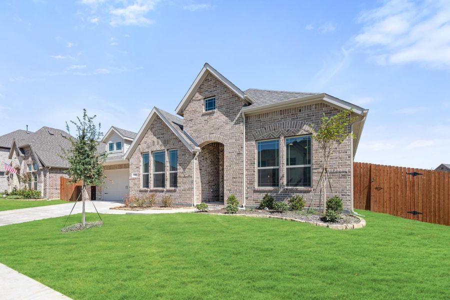 Two-story brick home with arched entry, attached garage, and manicured front lawn in a suburban neighborhood