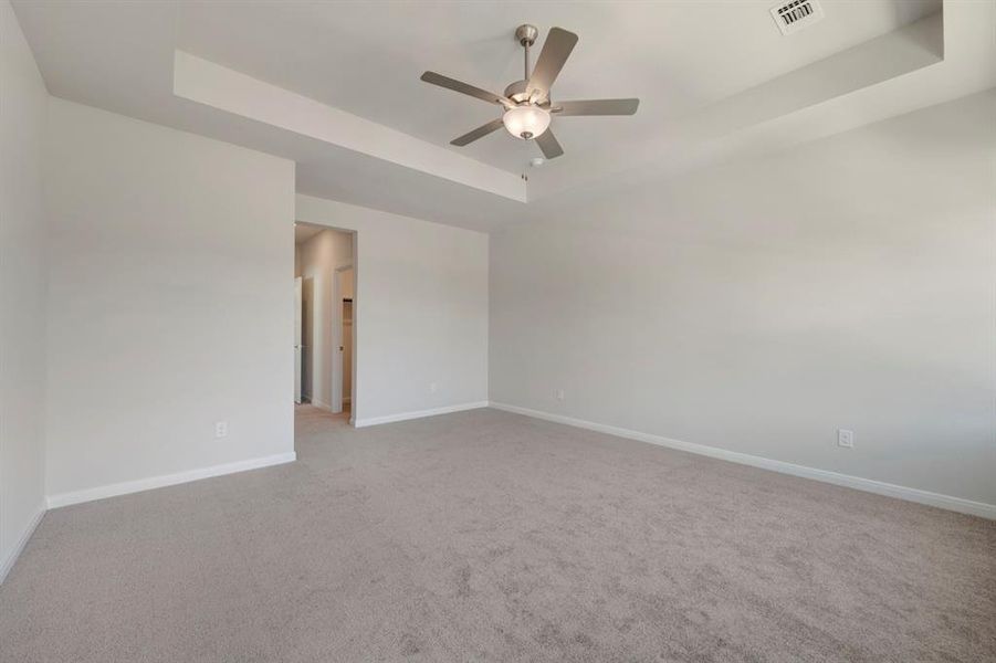 Empty room with a raised ceiling, light carpet, and ceiling fan
