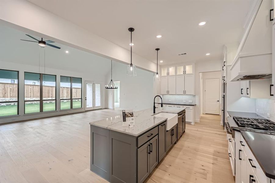 Kitchen with decorative backsplash, an island with sink, sink, pendant lighting, and white cabinetry