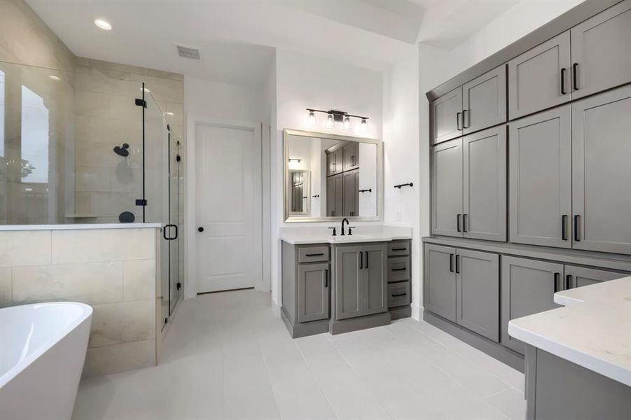 The bathroom features a freestanding bathtub, a glass-enclosed shower with black fixtures, and extensive gray cabinetry with black hardware