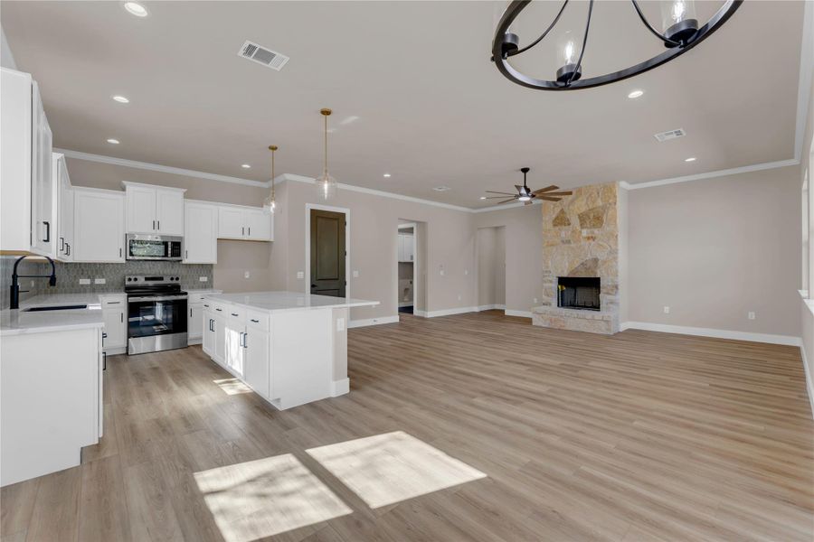 Kitchen featuring white cabinets, stainless steel appliances, a stone fireplace, hanging lights, and light wood-type flooring