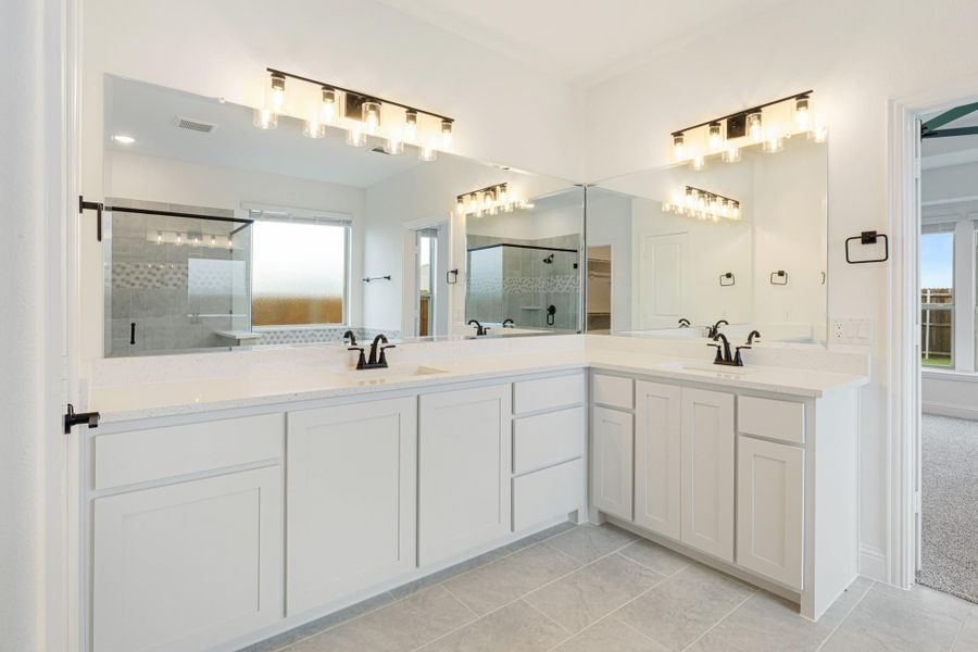 Master bathroom with dual sinks, L-shaped white vanity, large mirrors, and a glass-enclosed shower in the background.
