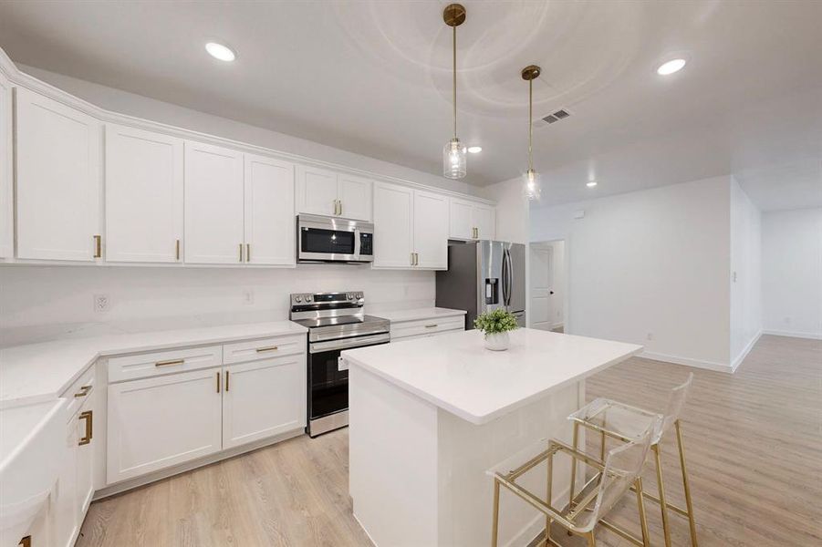 Kitchen featuring appliances with stainless steel finishes, light wood-type flooring, pendant lighting, white cabinets, and a kitchen island