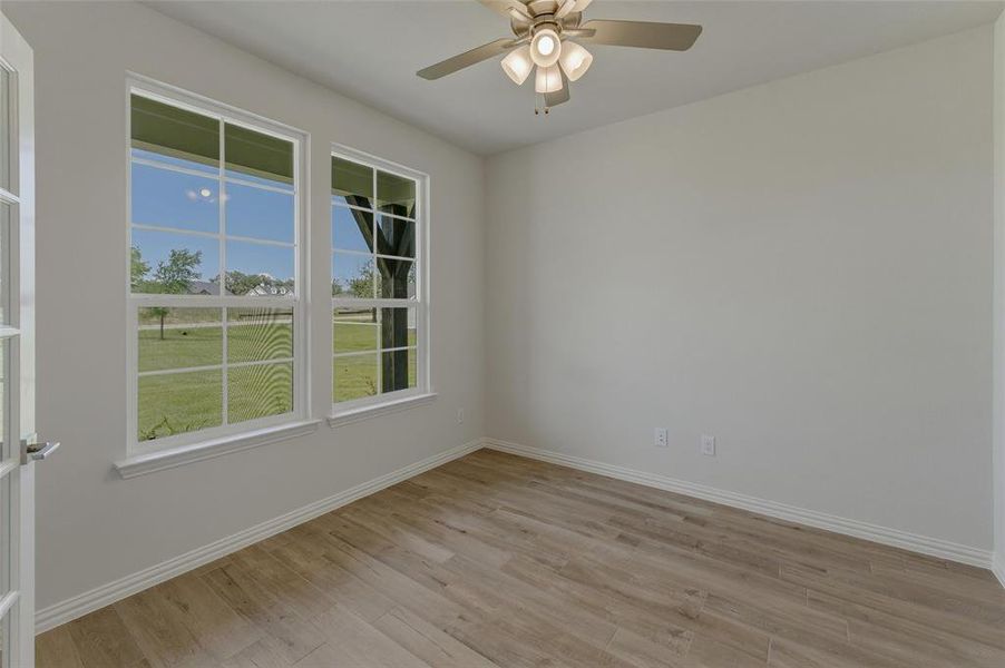 Room featuring light wood-finish flooring, two large multi-pane windows, a ceiling fan with integrated lighting, and white baseboards