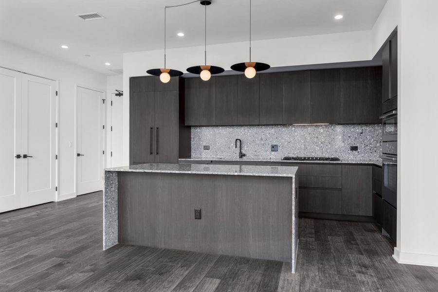 Kitchen featuring custom Italkraft cabninetry, terrazzo backsplash, waterfall-edge terrazzo countertops, built-in stainless steel Bosch appliances, and pendant lighting above kitchen island.