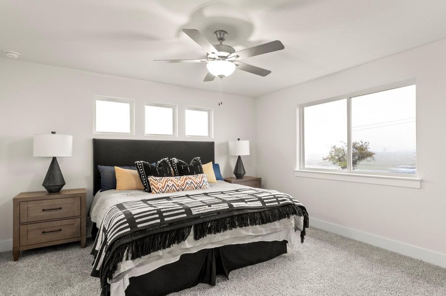 A comfortable bedroom features a ceiling fan, soft carpeting, and abundant natural light.