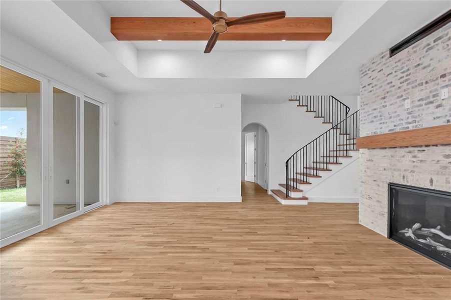 Unfurnished living room featuring a fireplace, a ceiling fan, light wood finished floors, arched walkways, and beam ceiling