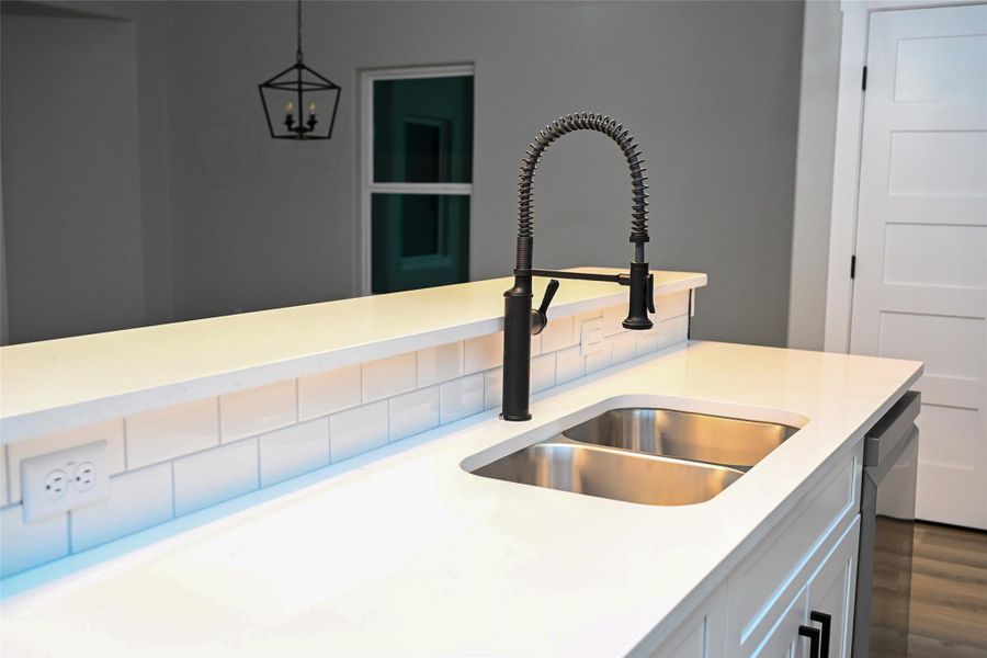 Kitchen view of hanging light fixtures, white cabinetry, stainless steel dishwasher, light stone counters, and dark wood-style floors