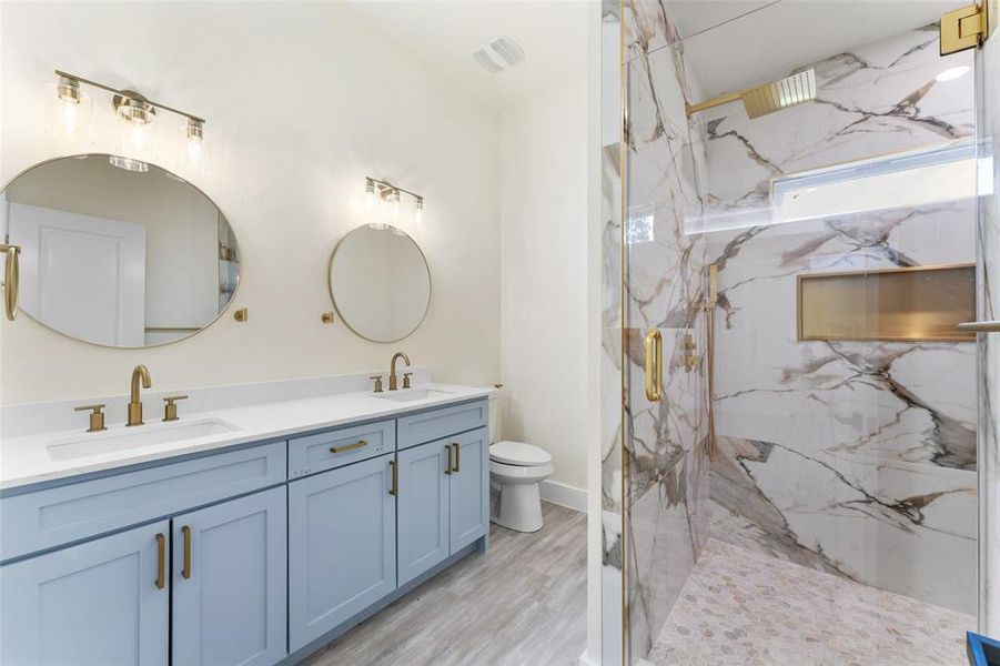 Full bath with double vanity, a marble finish shower, and wood finished floors