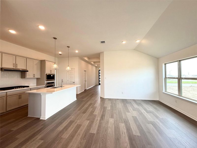 Kitchen with light countertops, wood finished floors, backsplash, an island with sink, and open floor plan Kitchen with light countertops, wood finished floors, backsplash, an island with sink, and open floor plan