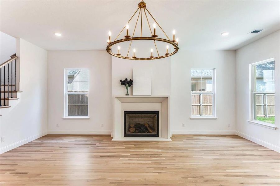 Unfurnished living room with light wood finished floors, stairs, a fireplace with flush hearth, recessed lighting, and a chandelier