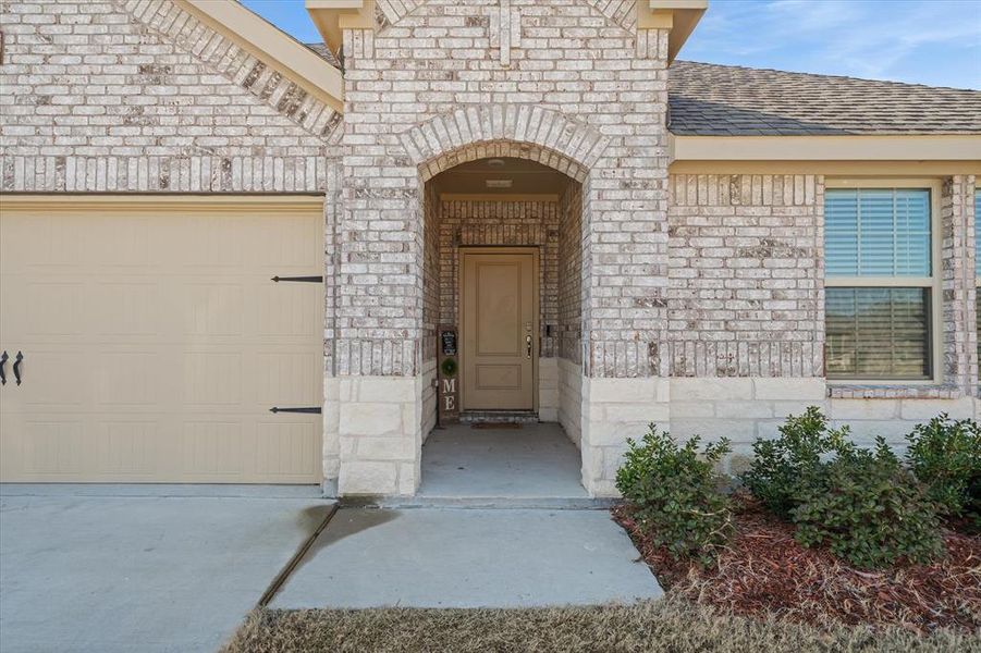 Entrance to property with an attached garage, driveway, brick siding, stone siding, and roof with shingles Entrance to property with an attached garage, driveway, brick siding, stone siding, and roof with shingles