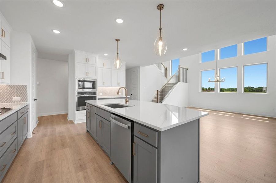 Modern kitchen with two-tone cabinetry, a central island featuring a sink and dishwasher, and built-in stainless steel appliances