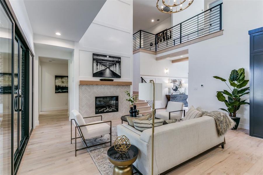 Living room with a high ceiling, a tiled fireplace, an inviting chandelier, and light wood-type flooring