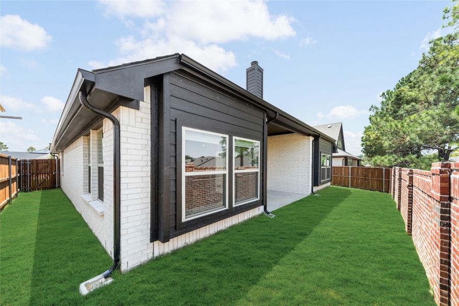 Backyard of single-story home with white brick exterior, dark trim, large windows, and fenced green lawn