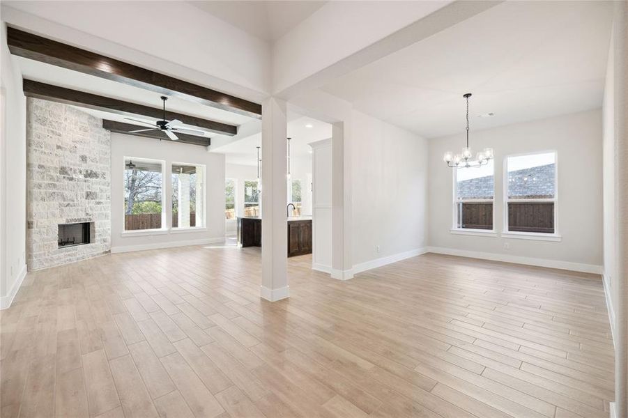 Unfurnished living room with a stone fireplace, beamed ceiling, ceiling fan with notable chandelier, and light wood-type flooring