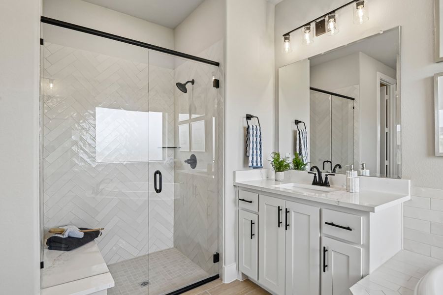 Bathroom with glass walk-in shower, herringbone tile, white vanity, and black fixtures