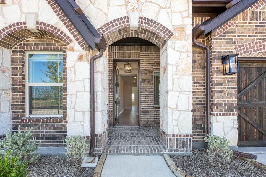 Home entrance with brick and stone arched doorway, open front door, and brick porch steps Home entrance with brick and stone arched doorway, open front door, and brick porch steps