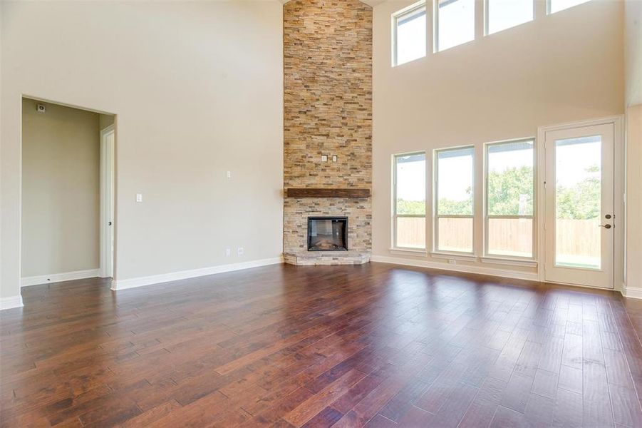 Unfurnished living room featuring a high ceiling, dark hardwood / wood-style floors, a stone fireplace, and a healthy amount of sunlight