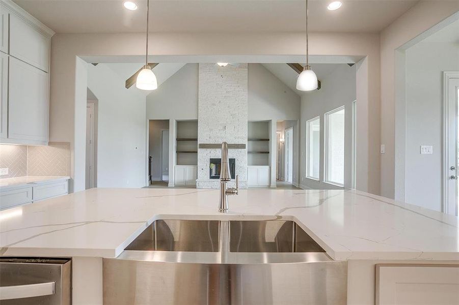 Kitchen with a fireplace, decorative backsplash, light stone countertops, white cabinetry, and hanging light fixtures