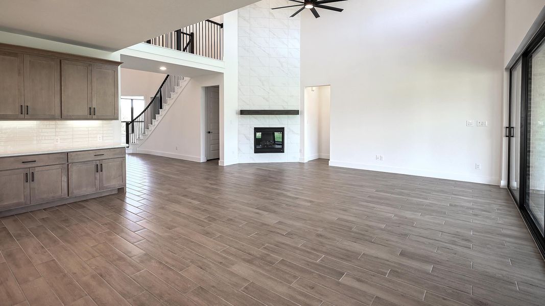 Unfurnished living room with a ceiling fan, dark wood-style floors, a tile fireplace, a high ceiling, and plenty of natural light Unfurnished living room with a ceiling fan, dark wood-style floors, a tile fireplace, a high ceiling, and plenty of natural light