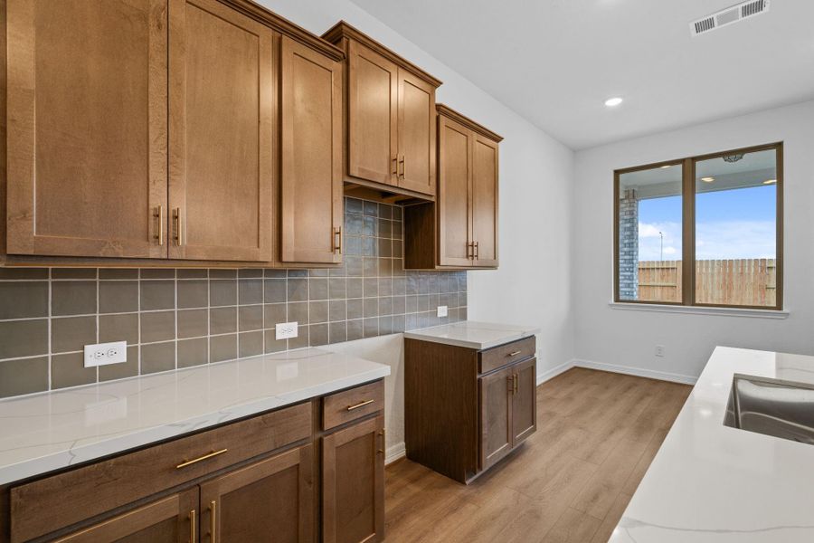 A close up showcasing the thoughtful details, from the gold hardware, unique backsplash, and natural stained cabinets.