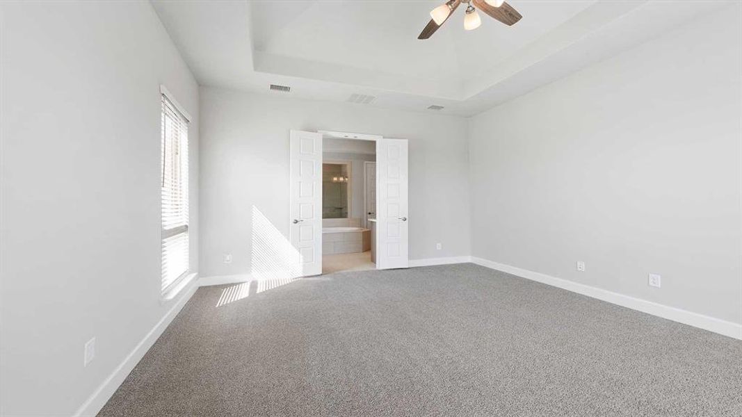 Empty room with carpet floors, a raised ceiling, and ceiling fan