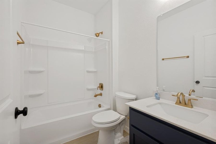 Bathroom featuring a white bathtub with integrated shower, brass-finish fixtures, a navy vanity with a white countertop, and a rectangular mirror
