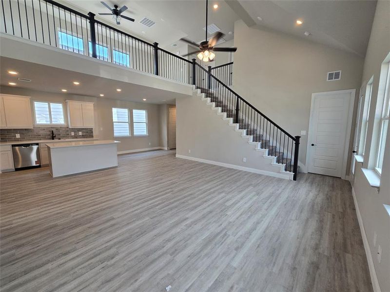 Unfurnished living room featuring stairway, a towering ceiling, light wood-type flooring, recessed lighting, and a ceiling fan