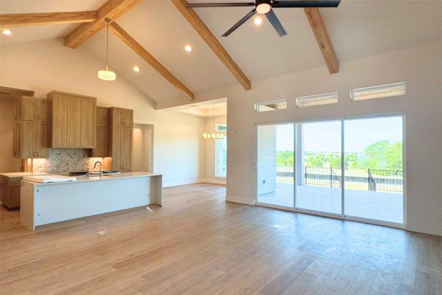 Kitchen featuring high vaulted ceiling, open floor plan, backsplash, decorative light fixtures, and a center island with sink