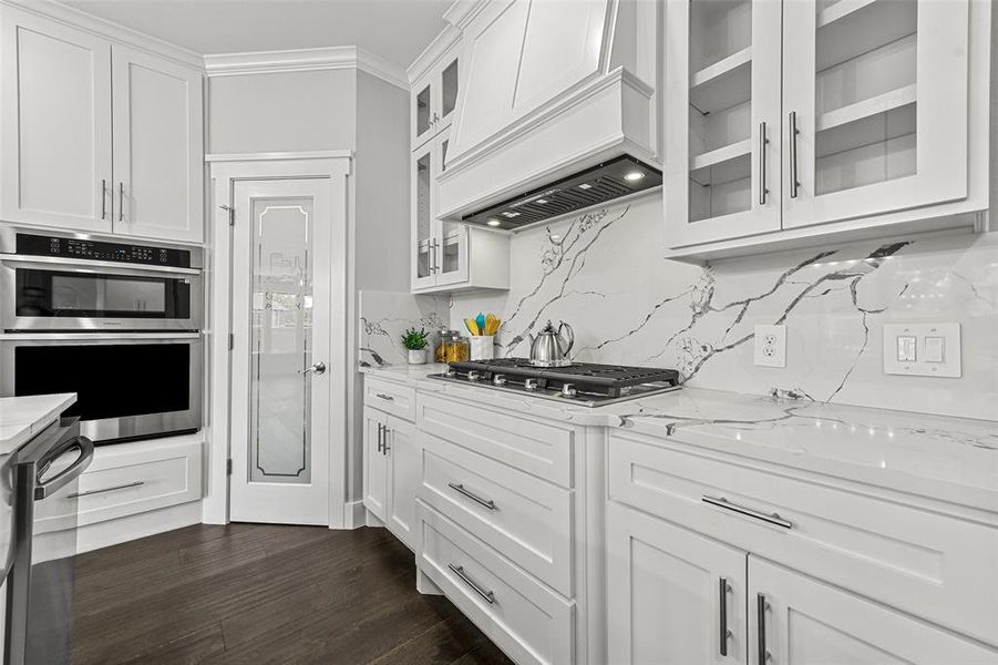 Kitchen featuring white cabinets, custom range hood, stainless steel appliances, and backsplash