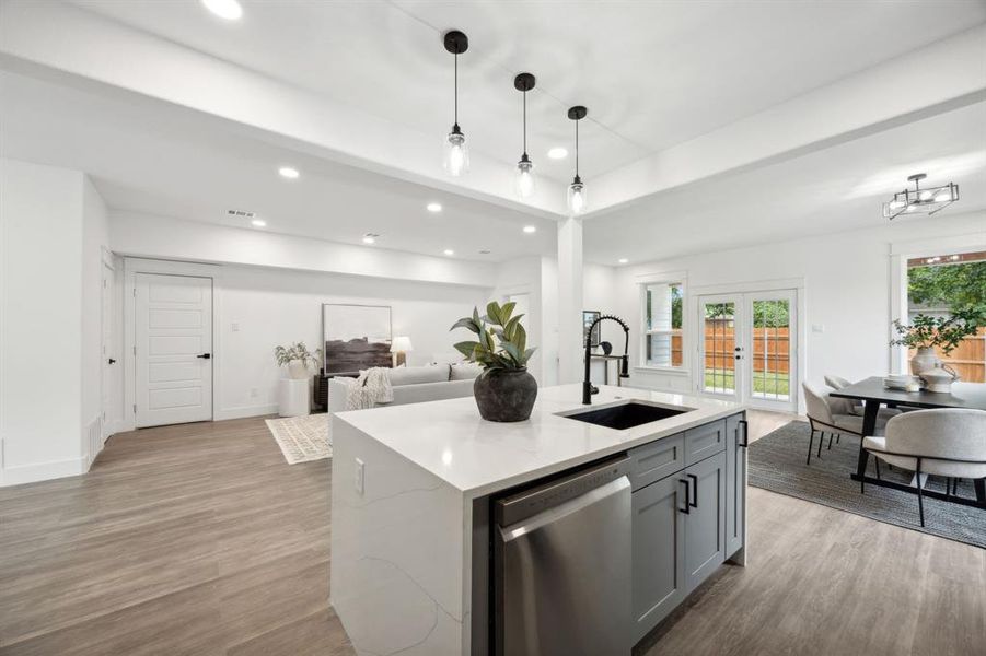 Kitchen with gray cabinetry, a center waterfall island with sink, stainless steel appliances and a pantry