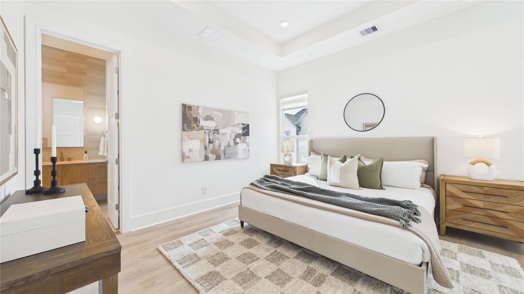 This bright bedroom features a modern design with neutral tones, a comfortable bed, stylish nightstands, and a cozy rug. It includes an attached bathroom and has ample natural light.