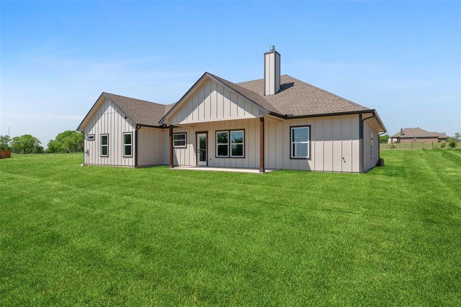 Rear view of property with a chimney, roof with shingles, a yard, and a patio