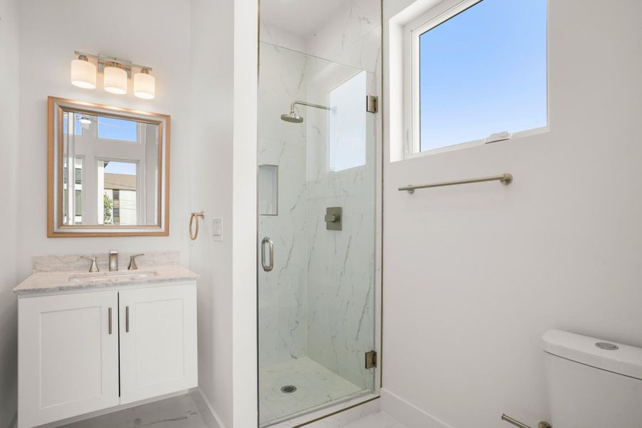 A well-lit full guest bathroom featuring a glass-enclosed shower and a vanity with marble counters. A well-lit full guest bathroom featuring a glass-enclosed shower and a vanity with marble counters.