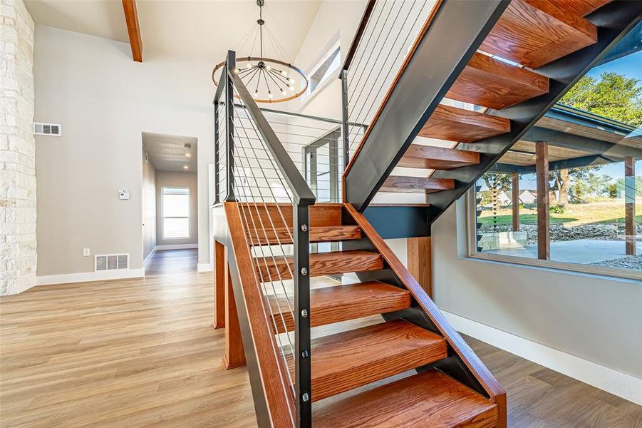Staircase with beam ceiling, wood finished floors, a chandelier, and a high ceiling Staircase with beam ceiling, wood finished floors, a chandelier, and a high ceiling