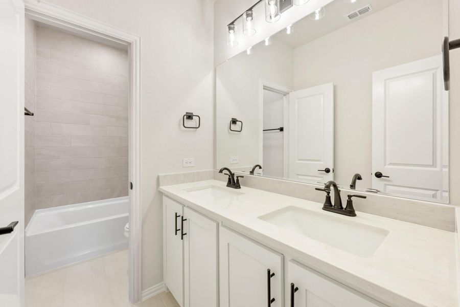 Bathroom with double sink vanity, white cabinets, large mirror, and tiled shower-tub combo