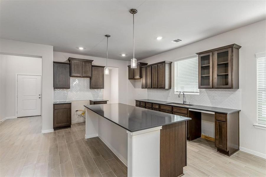 The heart of the home, this stunning kitchen features a large island, custom backsplash, and sleek countertops. The dark cabinetry provides ample storage, and the open design allows for easy interaction with the living and dining areas. Perfect for entertaining and everyday living, this kitchen is a chef's dream. Photos are from another Rylan floor plan.