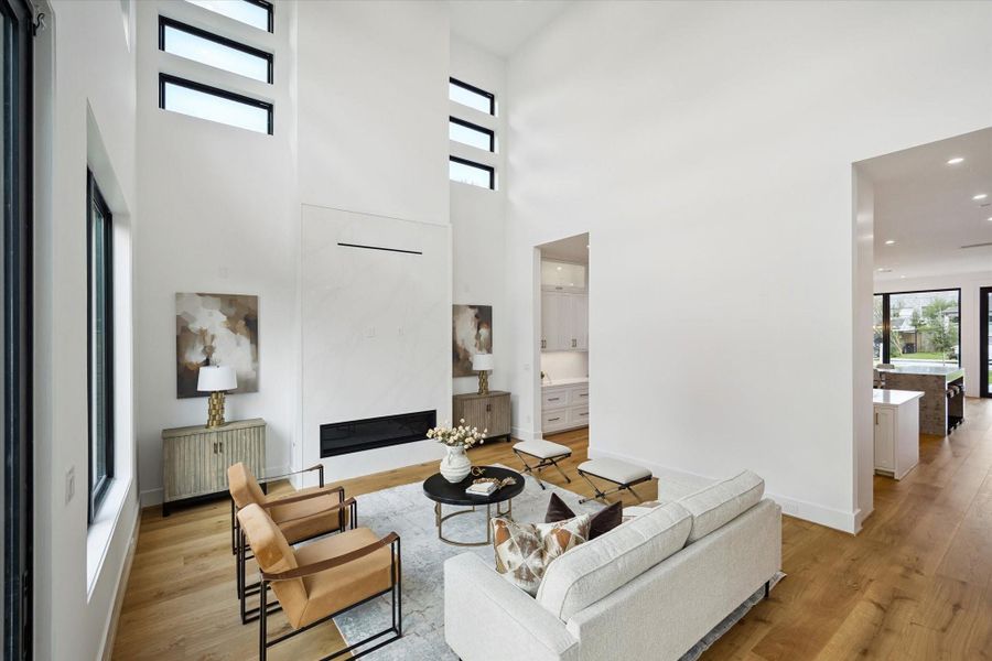 Bright living room with soaring ceilings and expansive windows. The focal point features a gas fireplace with an accent wall wrapped with a Quartz slab. Bright living room with soaring ceilings and expansive windows. The focal point features a gas fireplace with an accent wall wrapped with a Quartz slab.
