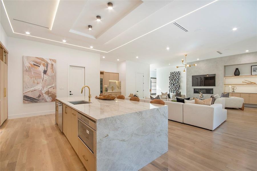 Kitchen featuring light stone countertops, light wood finished floors, modern cabinets, an island with sink, and light brown cabinets