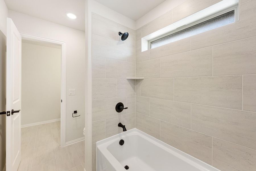 Bathtub and shower combo with large beige tiles, black fixtures, and a small frosted window above Bathtub and shower combo with large beige tiles, black fixtures, and a small frosted window above