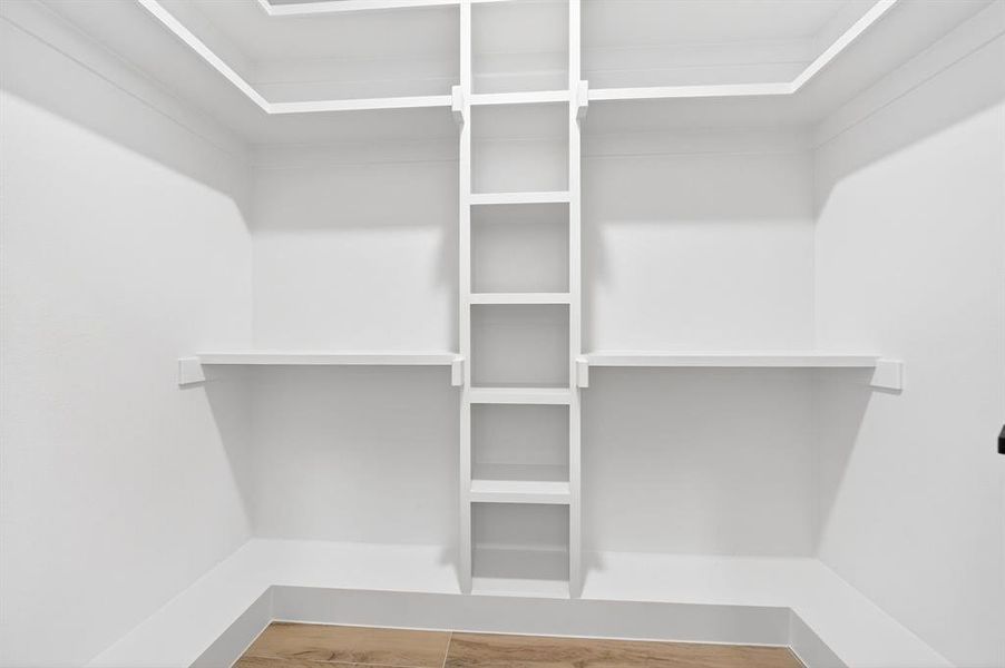 Walk-in closet with built-in shelving, white walls, and wood-finish flooring Walk-in closet with built-in shelving, white walls, and wood-finish flooring